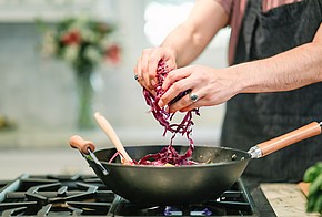 Person streut Rotkohl in Wok auf Gasherd