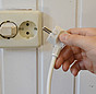 Weiße Wand mit Steckdose. Stecker wird gezogen.