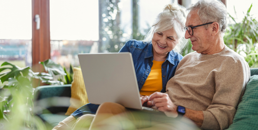 Älteres Ehepaar sitzt auf der Couch und schaut sich etwas auf dem Laptop an.